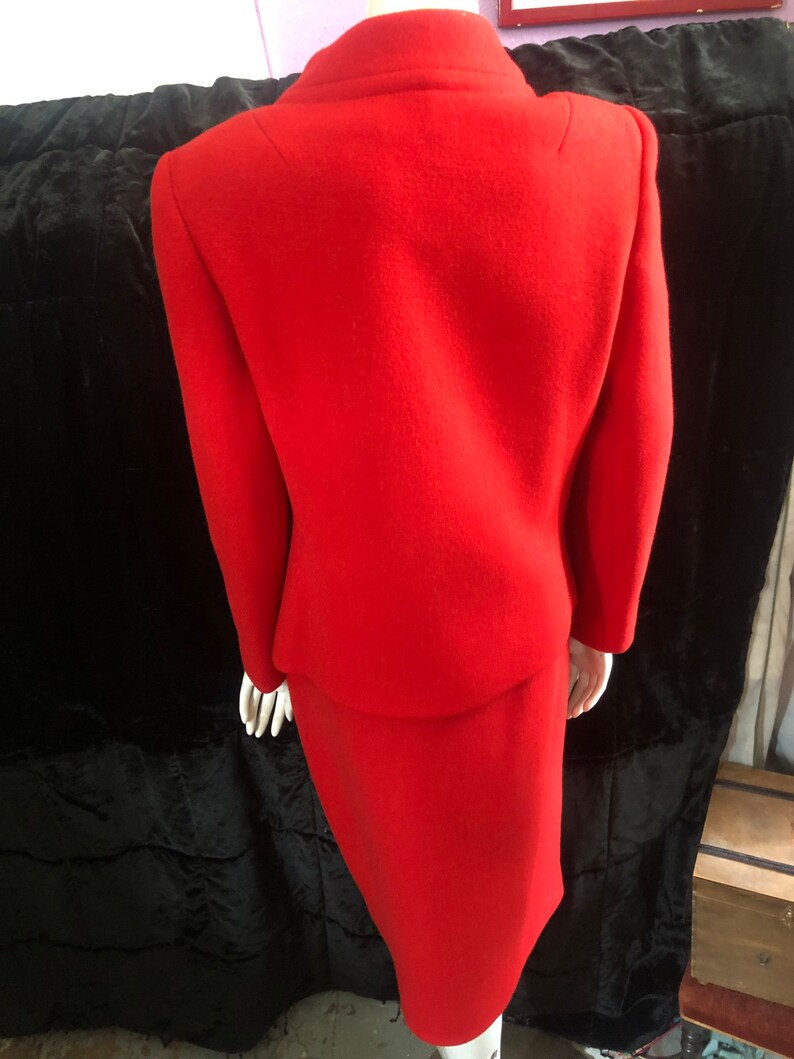 K&ouml;nnte beinhalten: Ein roter Wollrock-Anzug mit einem figurbetonten Rock und einer Jacke mit Stehkragen.