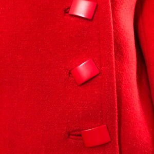 K&ouml;nnte beinhalten: Roter Wollmantel mit drei gro&szlig;en roten Plastikkn&ouml;pfen.