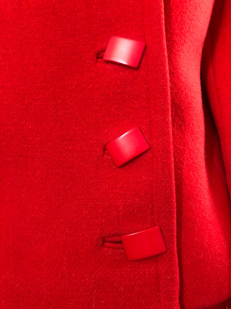 K&ouml;nnte beinhalten: Roter Wollmantel mit drei gro&szlig;en roten Plastikkn&ouml;pfen.