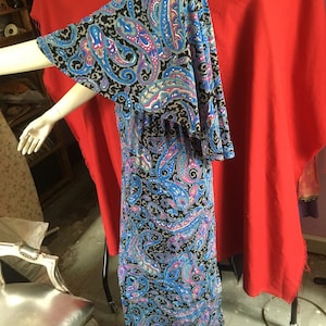May include: A long, flowing maxi dress with a paisley print in shades of blue, pink, and gray on a black background. The dress has a wide, flowing neckline and bell sleeves.
