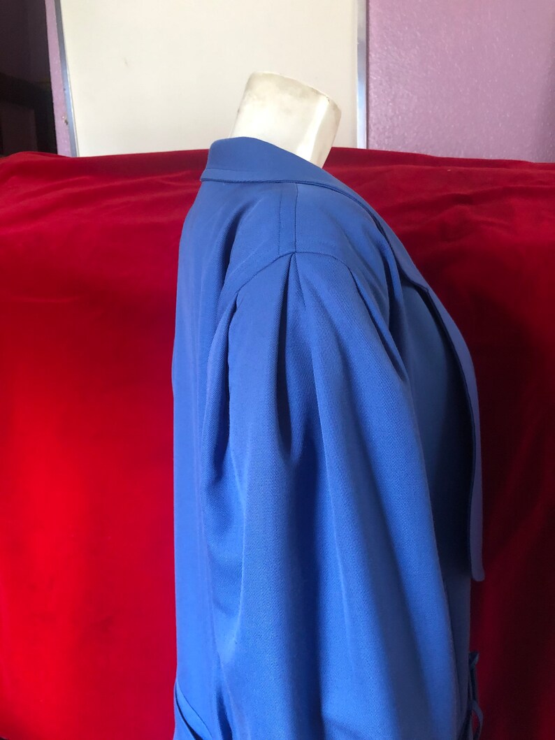 May include: A blue blazer with long sleeves and a collar. The blazer has a single button closure and a belt at the waist.