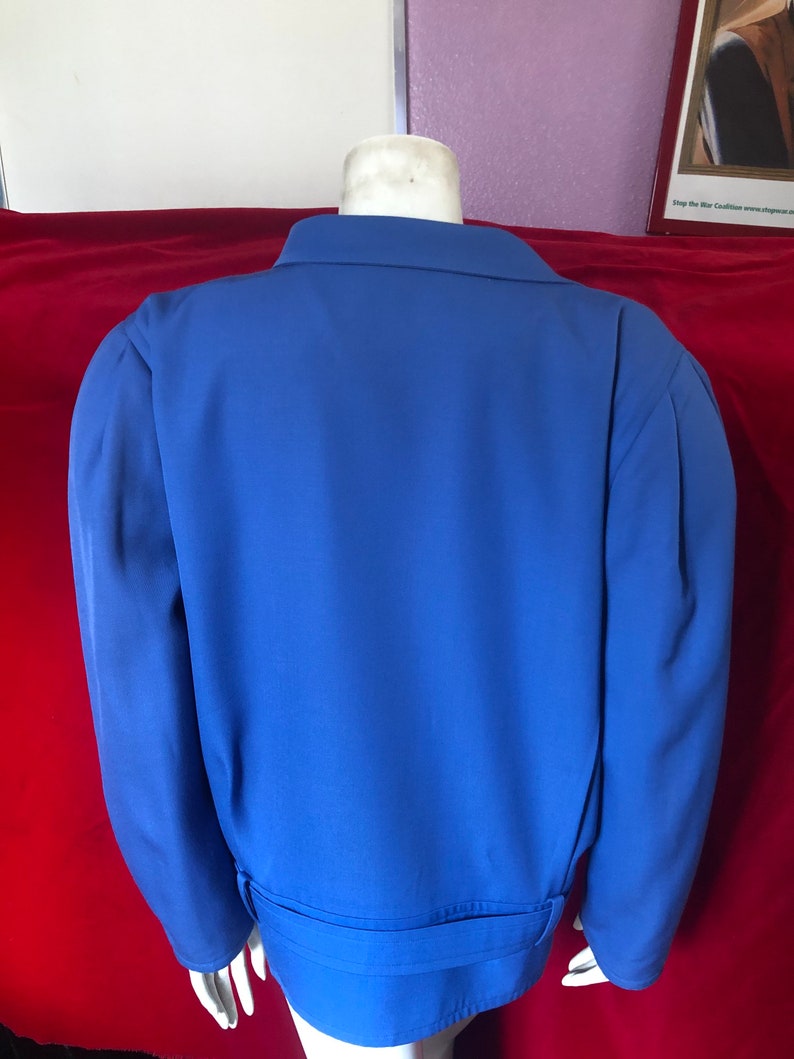 May include: A blue blazer with a belt. The blazer has long sleeves and a collar.