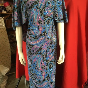 May include: A long, flowing maxi dress with a paisley print in shades of blue, pink, and black. The dress has a scoop neck and short sleeves.