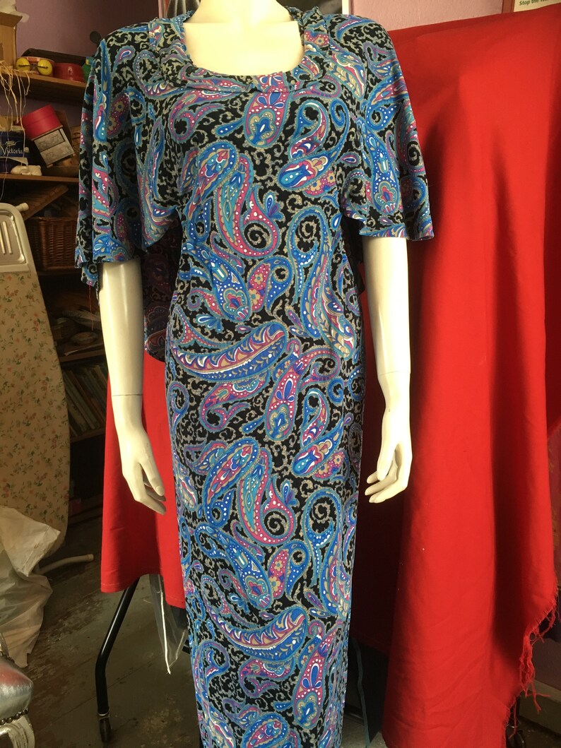 May include: A long, flowing maxi dress with a paisley print in shades of blue, pink, and black. The dress has a scoop neck and short sleeves.