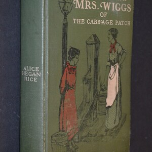 May include: A vintage hardcover book titled "Lovey Mary" by Alice Hegan Rice. The cover is green with illustrations of two women and a water pump. The book's spine displays the title and author's name.