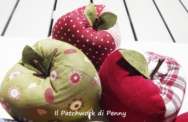 May include: Three handmade fabric apples in red, green, and white with a patchwork design. The apples have a stem and leaf made of felt.