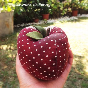 May include: A red fabric apple with white polka dots. The apple has a green felt leaf and a brown stem.