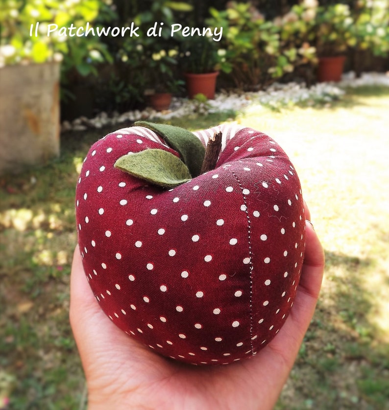 May include: A red fabric apple with white polka dots. The apple has a green felt leaf and a brown stem.