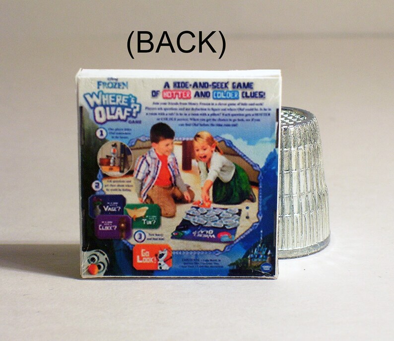 May include: A Frozen Where's Olaf game box with a blue and white background. The box features a picture of two children playing the game, with the text "A Kids-And-Seek Game of Hotter and Colder Clues!" on the front.