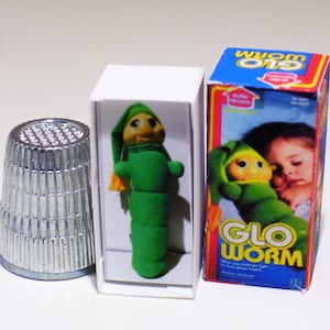 May include: A miniature box of a green glow-in-the-dark worm toy. The box has a picture of a child sleeping with the toy. The text on the box reads "Glo Worm".