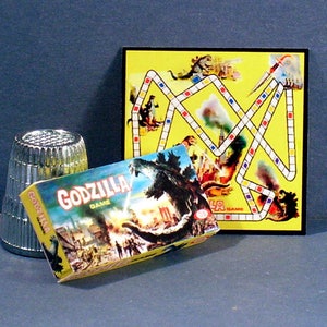 May include: A vintage Godzilla board game with a yellow game board and a box featuring a Godzilla illustration. The game board has a path with colored squares and images of Godzilla and other monsters. The box is yellow and red with the words "Godzilla Game" printed on it.