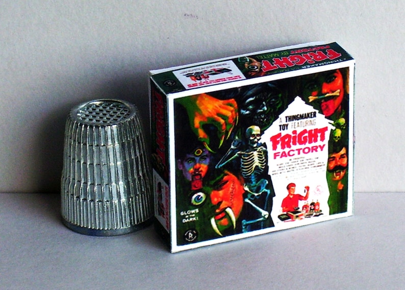 May include: A Fright Factory Thingmaker toy box with a white background and colorful illustrations. The box features a skeleton, a monster with fangs, and a person with a glowing eye. The text on the box reads 'A Thingmaker Toy Featuring Fright Factory'. The box is made of cardboard and has a red, white, and blue color scheme.