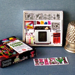 K&ouml;nnte beinhalten: Ein Vintage-Bastelset von Creepy Peeple mit einer schwarz-wei&szlig;en Schachtel mit bunten Illustrationen von Monstern und einer wei&szlig;en Schachtel mit einem Projektor, Farbe und Stempeln. Das Set enth&auml;lt auch eine Bogen mit Aufklebern in verschiedenen Monsterformen.