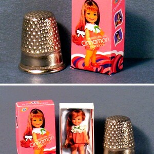 May include: A vintage doll in a pink and white box with the words "Little Miss Cinnamon" on the front. The doll is wearing a red and white dress and has long brown hair. The box is next to a silver thimble.