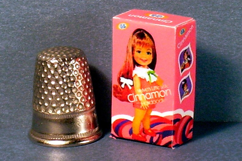 May include: A pink box with a doll on the front. The doll has long red hair and is wearing a pink dress with a green bow. The box says "What's Like Box Cinnamon Hairdo's".