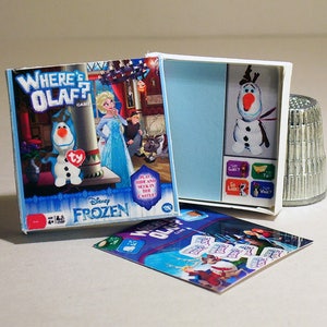 May include: A Disney Frozen Where's Olaf? game with a blue and white box featuring Olaf the snowman. The game includes a plush Olaf figure and a game board with different locations to hide Olaf.