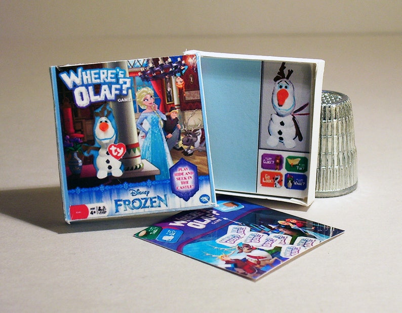 May include: A Disney Frozen Where's Olaf? game with a blue and white box featuring Olaf the snowman. The game includes a plush Olaf figure and a game board with different locations to hide Olaf.
