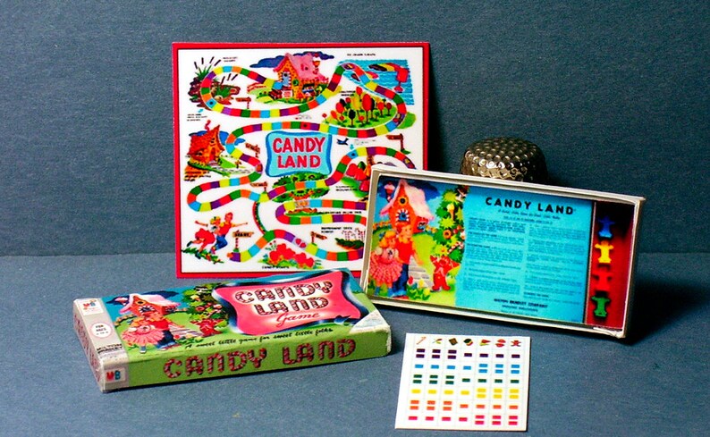 Pu&ograve; includere: Un gioco da tavolo vintage di Candy Land con un tabellone di gioco colorato, pedine e istruzioni. Il tabellone di gioco presenta un percorso tortuoso con caselle a tema caramelle. Le pedine sono piccole figure colorate. Le istruzioni sono stampate su una carta blu.