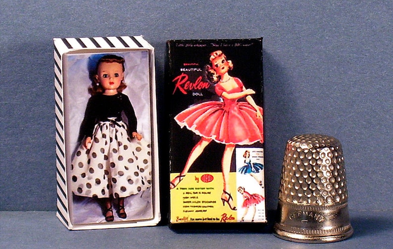 May include: Two boxes of vintage Revlon dolls. One box features a doll in a black top and white polka dot skirt. The other box features a doll in a red dress. The boxes are on a blue surface with a silver thimble.