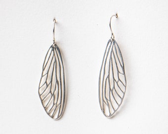 May include: A pair of silver earrings with a delicate, intricate design resembling a dragonfly wing.