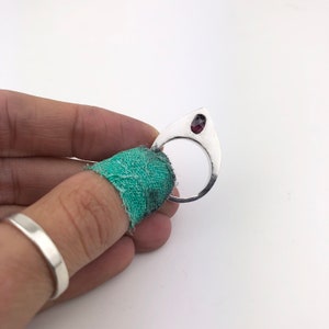 May include: A silver ring with a teardrop-shaped design and a red gemstone set in the top.