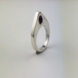 May include: A silver ring with a black gemstone set in a pointed, triangular design.