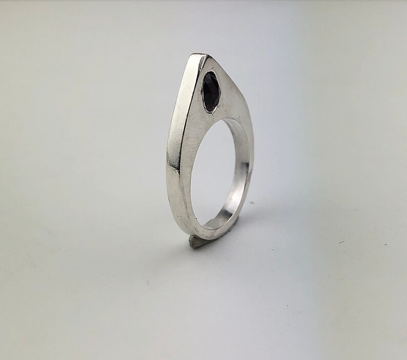 May include: A silver ring with a black gemstone set in a pointed, triangular design.