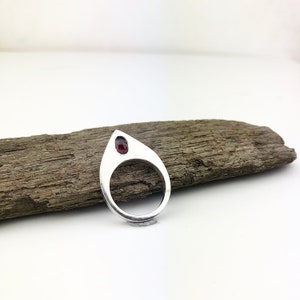 May include: A silver ring with a teardrop-shaped design and a red gemstone set in the center.