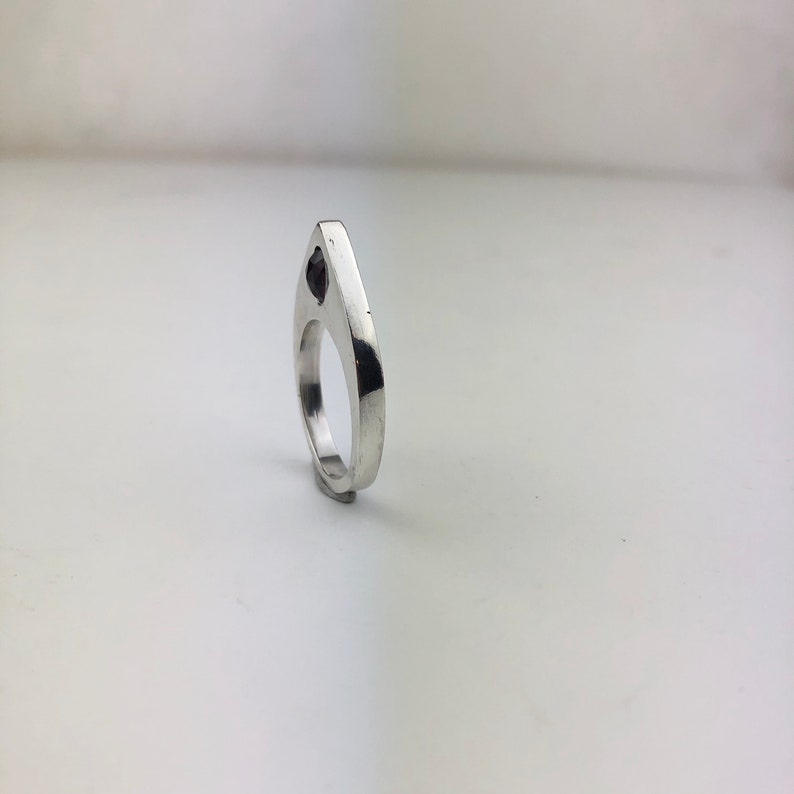 May include: A silver ring with a black stone set in the center. The ring is shaped like a teardrop and has a smooth, polished finish.