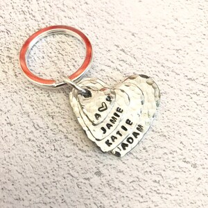 May include: Silver heart-shaped keyring with the names Jamie, Katie, and Adam engraved on it. The keyring has a small heart charm with the word "Love" engraved on it.