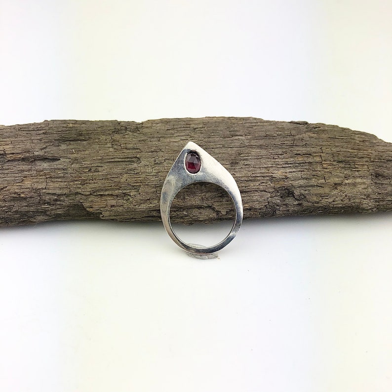 May include: A silver ring with a teardrop-shaped design and a red gemstone set in the center.