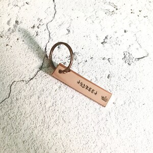 May include: A rose gold keychain with a rectangular tag that says "ANDREEA" with a small crown symbol.