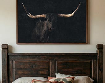 May include: A framed black and white print of a longhorn bull. The bull's dark coat contrasts with its large, curved horns, set against a dark background. The artwork is displayed above a wooden headboard with pillows.