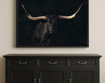 May include: A rectangular wall art print featuring a dark, moody portrait of a longhorn bull with prominent, sweeping horns. The bull is black, set against a deep, textured black background, and framed in a thin, dark-colored frame.