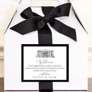 May include: White gift box with a black ribbon and bow. A black framed card on the front reads "Welcome" with a message and the names "Nicole & Adam". The box has a handle for carrying.
