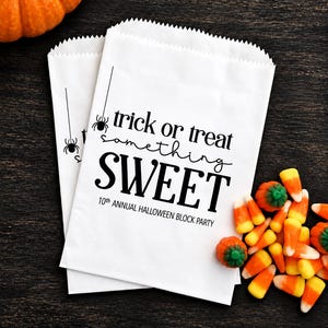 May include: Two white paper bags with serrated top edges featuring black text that reads trick or treat something SWEET 10th ANNUAL HALLOWEEN BLOCK PARTY and a small spider graphic hanging from a vertical line on the left side of the bags.