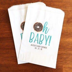 May include: Two white paper bags with a blue and white donut graphic and the text "Oh Baby!"  Alicia's Baby Shower 04.21.18
