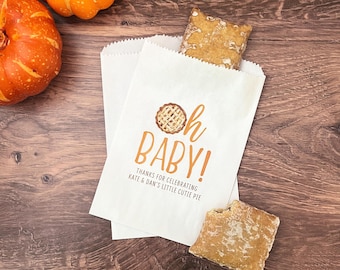 May include: White paper gift bags with a brown and orange pie design and the text "Oh Baby! Thanks for celebrating Kate & Dan's little cutie pie."