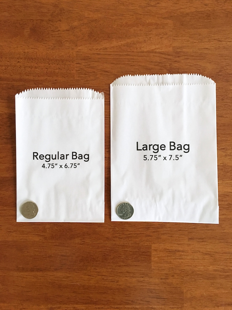 May include: Two white paper bags, labeled "Regular Bag" and "Large Bag." The regular bag measures 4.75" x 6.75", and the large bag is 5.75" x 7.5". A coin is placed next to each bag for size comparison. The bags are on a wooden surface.