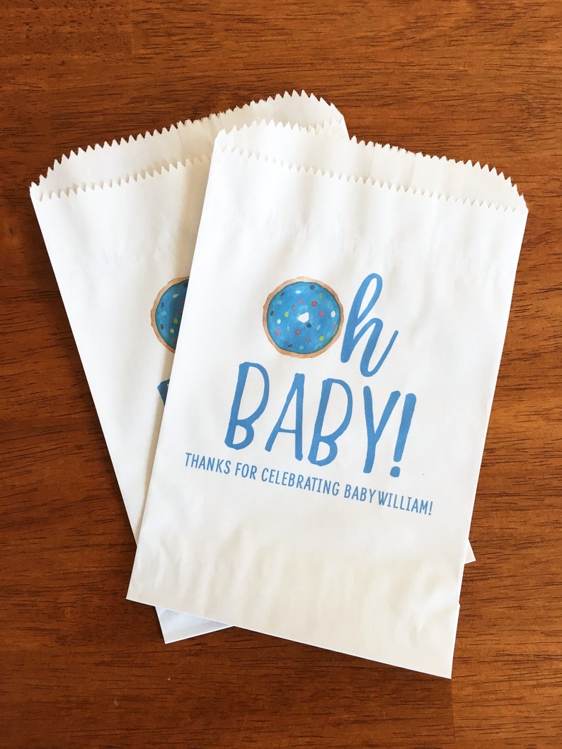 May include: Two white paper bags with blue and white text that reads "Oh Baby!" and "Thanks for celebrating Baby William!"  A blue and white donut with sprinkles is above the text.