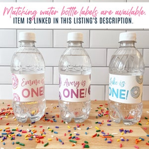 K&ouml;nnte beinhalten: Drei durchsichtige Plastikwasserflaschen mit personalisierten Etiketten f&uuml;r eine erste Geburtstagsfeier. Die Etiketten zeigen ein Donut-Design und den Text "Emma ist EINS!", "Avery ist EINS!" und "Luke ist EINS!"