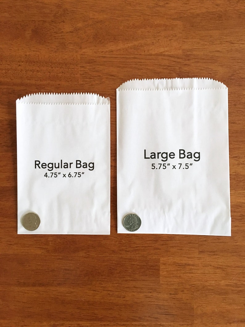 K&ouml;nnte beinhalten: Zwei wei&szlig;e Papiert&uuml;ten, eine mit der Aufschrift "Regular Bag 4.75" x 6.75"" und die andere mit der Aufschrift "Large Bag 5.75" x 7.5"". Eine US-amerikanische 25-Cent-M&uuml;nze liegt vor jeder T&uuml;te zur Gr&ouml;&szlig;envergleich.
