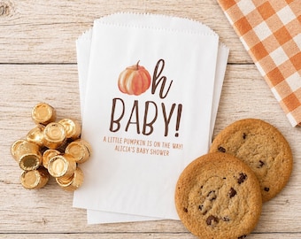 May include: White paper treat bags with a pumpkin graphic and the words "Oh Baby!" printed in brown. The bags are next to chocolate candies and chocolate chip cookies. A baby shower theme.