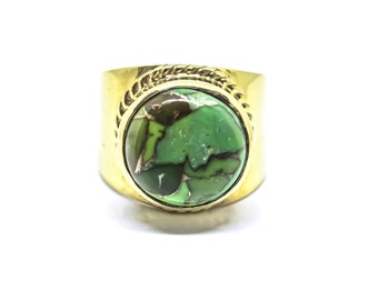 May include: A gold-toned ring featuring a large, round, polished green stone with dark brown matrix veining. The stone is set in a smooth bezel surrounded by a decorative twisted rope metal border, mounted on a wide, solid gold-toned band.