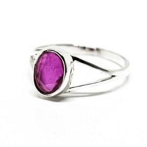 May include: A silver ring with a deep purple oval gemstone set in a bezel setting. The ring has a split shank.