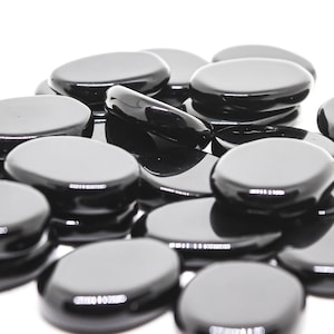 May include: A pile of smooth, black glass stones. The stones are oval shaped and have a glossy finish.