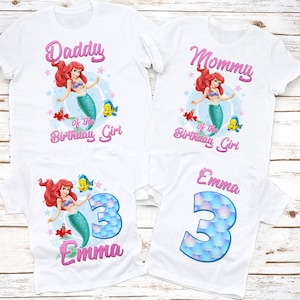 May include: Set of four white t-shirts with a mermaid theme. The shirts feature a pink and white design with the words "Daddy of the Birthday Girl", "Mommy of the Birthday Girl", "Emma" and a number "3" with a mermaid tail design.