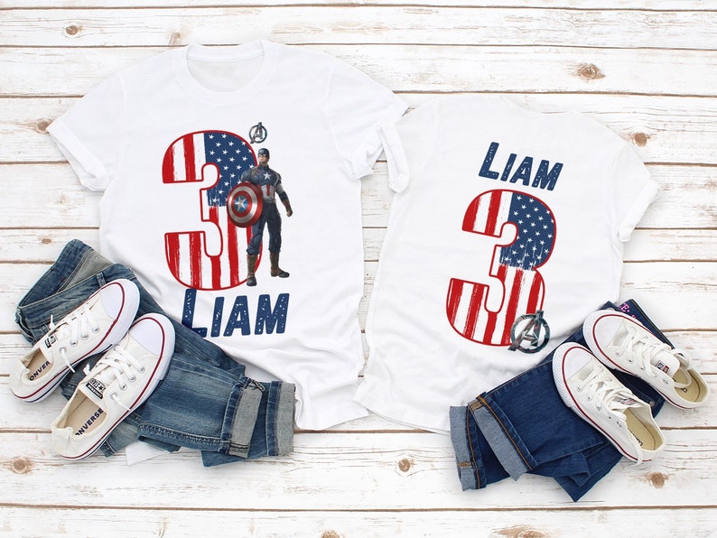 Peut inclure: T-shirts blancs avec un motif patriotique repr&eacute;sentant le chiffre 3 en rouge et bleu, avec le motif du drapeau am&eacute;ricain. Un t-shirt pr&eacute;sente un graphisme Captain America et le nom "Liam". Les t-shirts sont associ&eacute;s &agrave; des jeans bleus et des baskets blanches.
