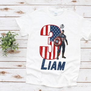 Peut inclure: T-shirt blanc avec un motif Captain America. Le chiffre "3" est orn&eacute; de rayures rouges et blanches et d'&eacute;toiles bleues, rappelant le drapeau am&eacute;ricain. Le nom "LIAM" est imprim&eacute; en bleu.