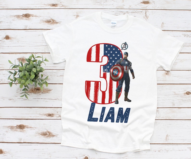 Peut inclure: T-shirt blanc avec un motif Captain America. Le chiffre "3" est orn&eacute; de rayures rouges et blanches et d'&eacute;toiles bleues, rappelant le drapeau am&eacute;ricain. Le nom "LIAM" est imprim&eacute; en bleu.